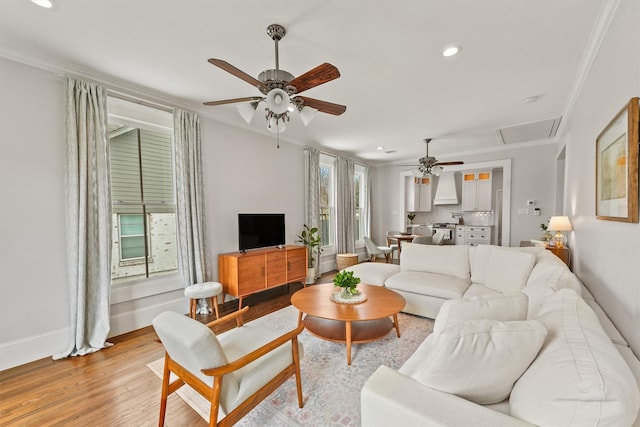 living room featuring a ceiling fan, attic access, light wood finished floors, ornamental molding, and recessed lighting