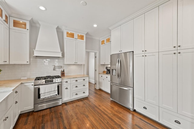 kitchen with dark wood-style flooring, backsplash, white cabinetry, custom range hood, and appliances with stainless steel finishes