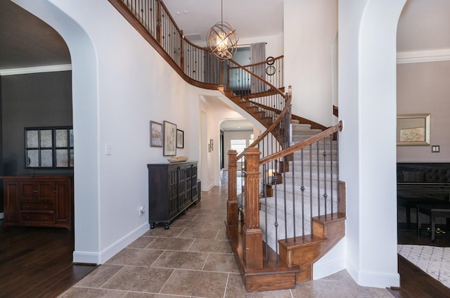 staircase featuring arched walkways, baseboards, ornamental molding, and a high ceiling