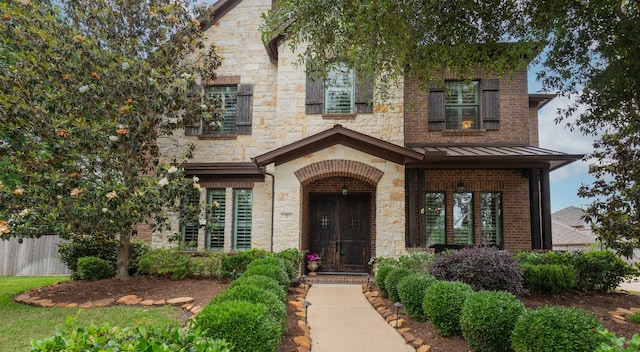 view of front facade featuring a standing seam roof, fence, brick siding, and stone siding