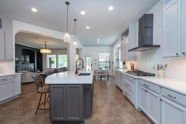 kitchen featuring decorative backsplash, a breakfast bar, wall chimney exhaust hood, arched walkways, and a sink