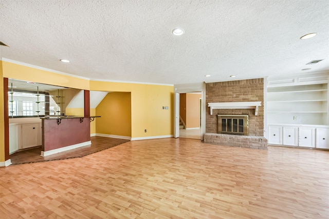9402 Stockport Dr, Spring, TX 77379 - unfurnished living room with a textured ceiling, light wood-style floors, ornamental molding, baseboards, and a brick fireplace