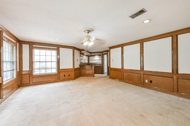 9402 Stockport Dr, Spring, TX 77379 - unfurnished living room with a decorative wall, ceiling fan, light carpet, wainscoting, and a textured ceiling