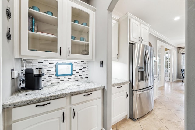 kitchen featuring white cabinets, stainless steel fridge, light tile patterned floors, tasteful backsplash, and glass insert cabinets