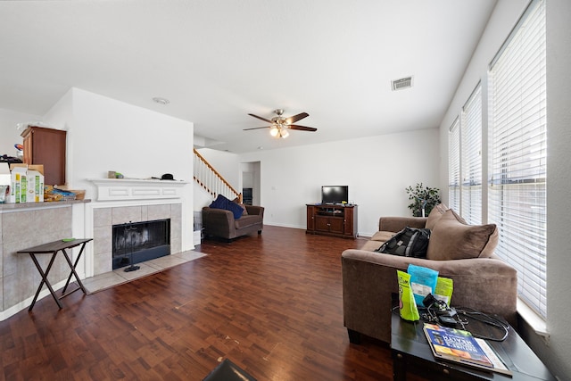 living area with stairs, wood finished floors, ceiling fan, a tiled fireplace, and visible vents
