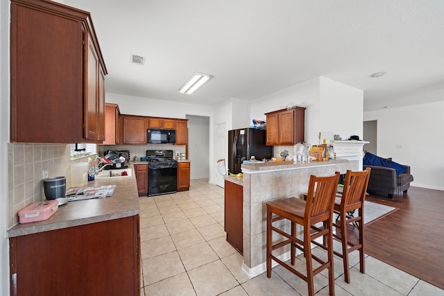 kitchen with visible vents, light tile patterned floors, a sink, black appliances, and a peninsula