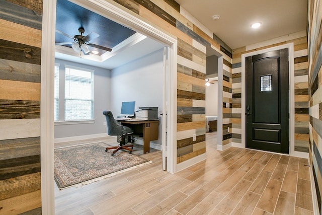 home office with baseboards, light wood-type flooring, a ceiling fan, and wood walls