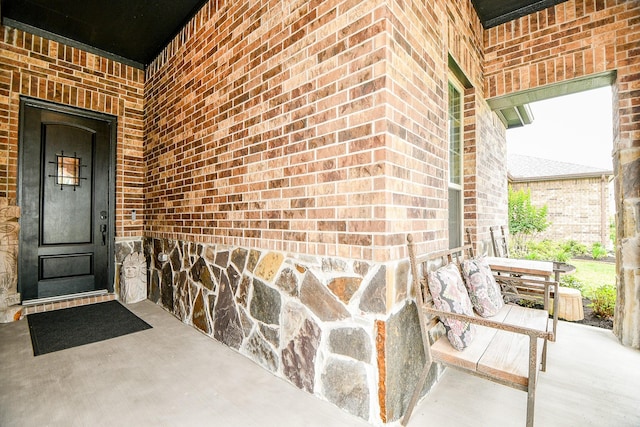 property entrance featuring a porch and brick siding