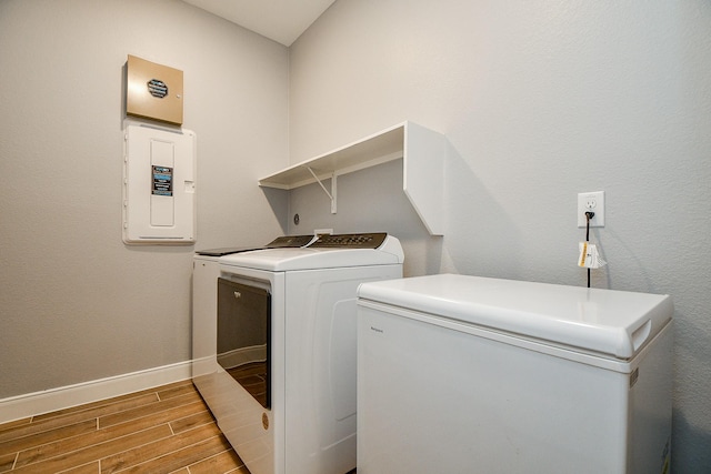 clothes washing area featuring laundry area, baseboards, wood finished floors, washing machine and dryer, and electric panel