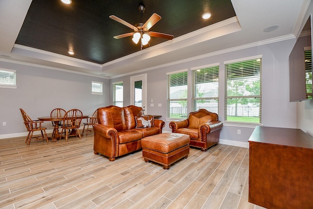 living room featuring ornamental molding, baseboards, ceiling fan, a tray ceiling, and light wood-style flooring