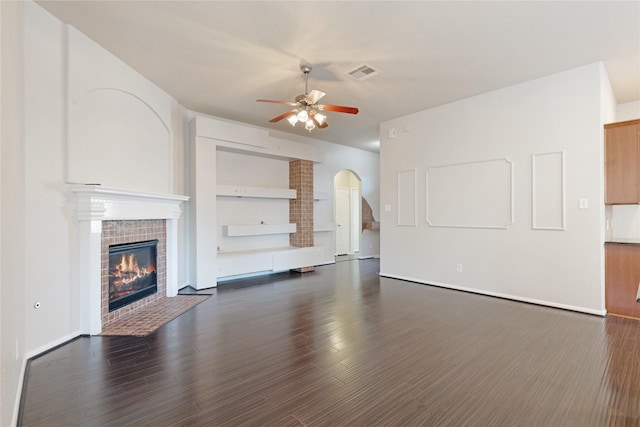 unfurnished living room featuring a tile fireplace, dark wood-style floors, visible vents, a ceiling fan, and arched walkways