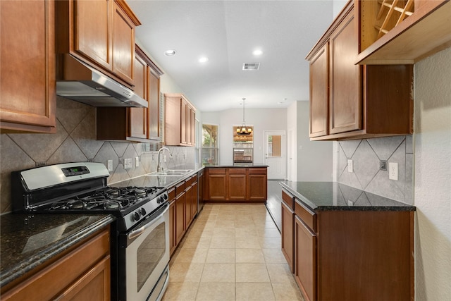 kitchen featuring dark stone countertops, a sink, stainless steel gas stove, under cabinet range hood, and visible vents