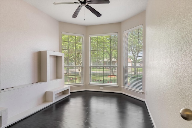 interior space featuring a textured wall, a ceiling fan, baseboards, and dark wood-style floors