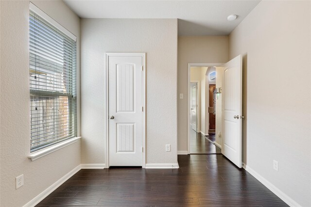 unfurnished bedroom with arched walkways, dark wood-type flooring, and baseboards