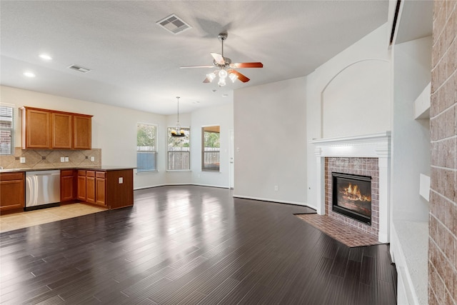 kitchen featuring open floor plan, dishwasher, ceiling fan, a tiled fireplace, and visible vents
