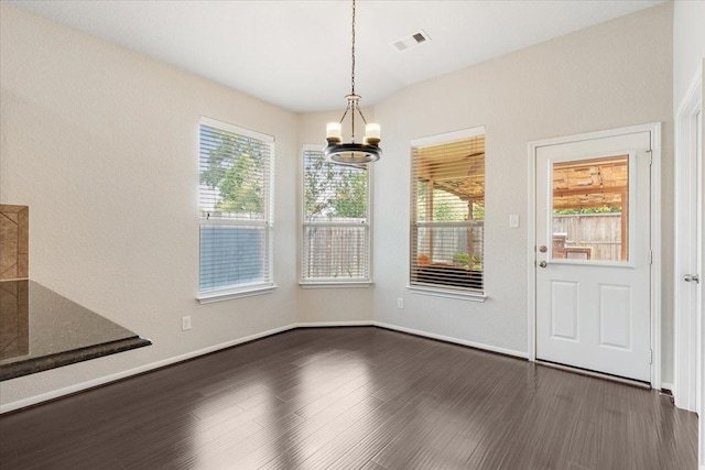 unfurnished dining area with dark wood-style flooring, visible vents, baseboards, and a notable chandelier