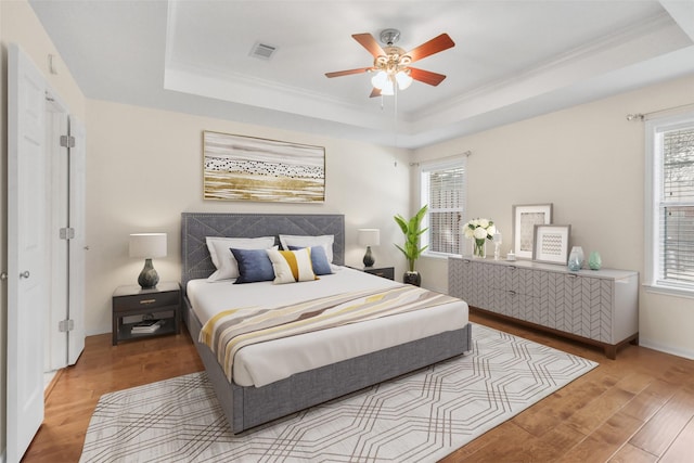 bedroom featuring visible vents, wood finished floors, a tray ceiling, and multiple windows