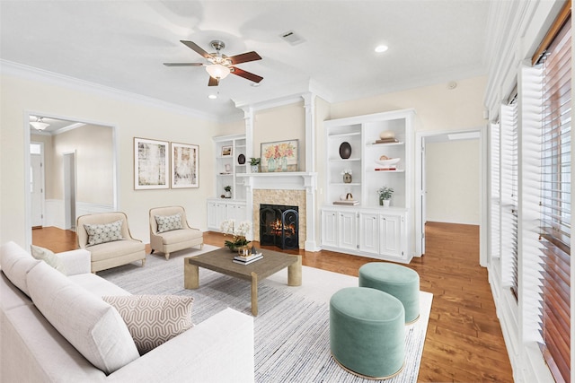 living room with crown molding, wood finished floors, ceiling fan, a lit fireplace, and visible vents