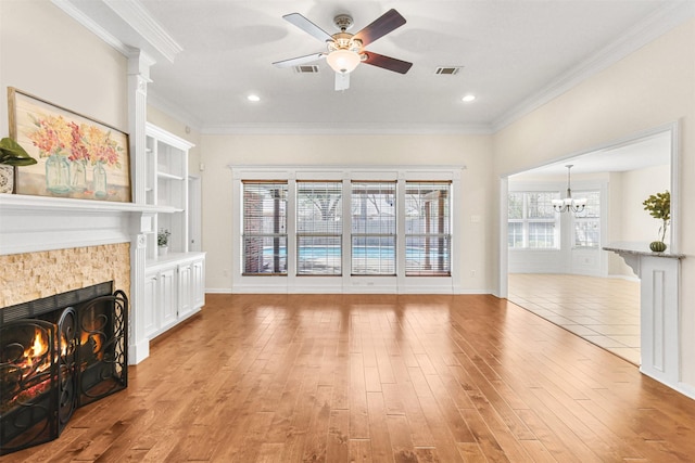 unfurnished living room with ceiling fan with notable chandelier, a tiled fireplace, visible vents, and ornamental molding