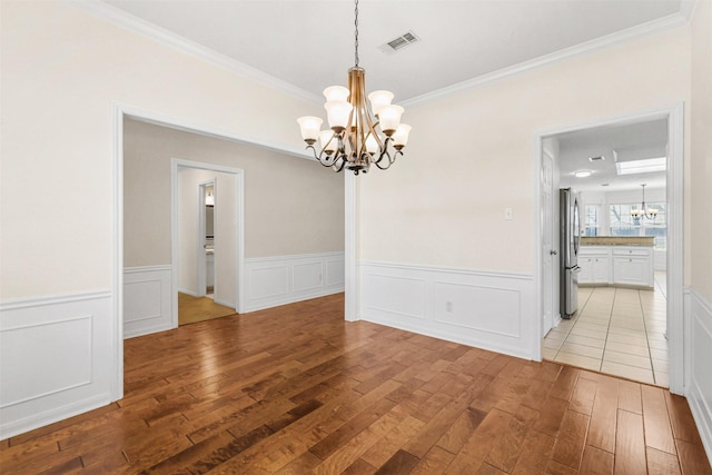 unfurnished dining area with a chandelier, light wood-style flooring, visible vents, and crown molding