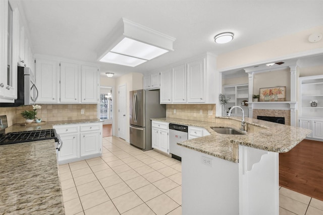 kitchen with white cabinets, light tile patterned floors, a sink, a peninsula, and appliances with stainless steel finishes