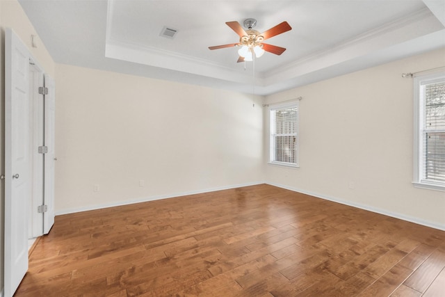 empty room with crown molding, hardwood / wood-style flooring, ceiling fan, a raised ceiling, and visible vents