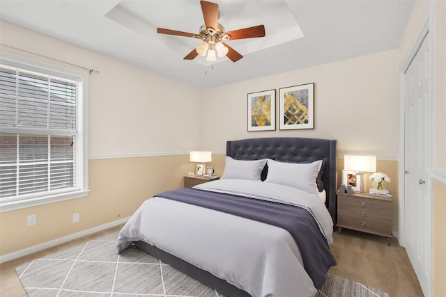 carpeted bedroom with a tray ceiling, a closet, baseboards, and ceiling fan