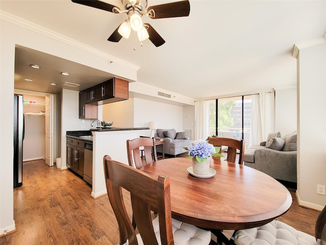 dining space featuring baseboards, visible vents, light wood-style floors, a ceiling fan, and crown molding