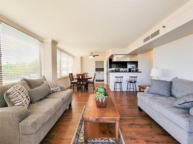living room with a ceiling fan, visible vents, ornamental molding, and dark wood-style flooring