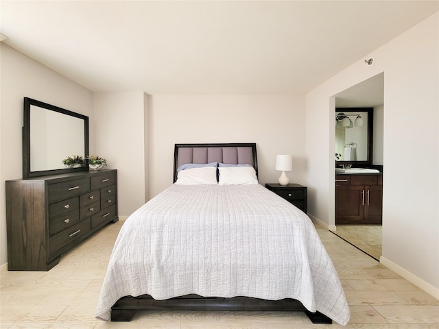 bedroom featuring baseboards, ensuite bathroom, light wood-type flooring, and a sink