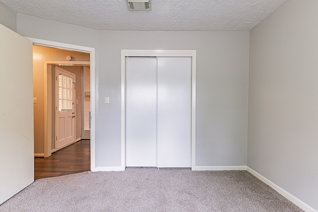 unfurnished bedroom featuring a textured ceiling, a closet, carpet, baseboards, and visible vents