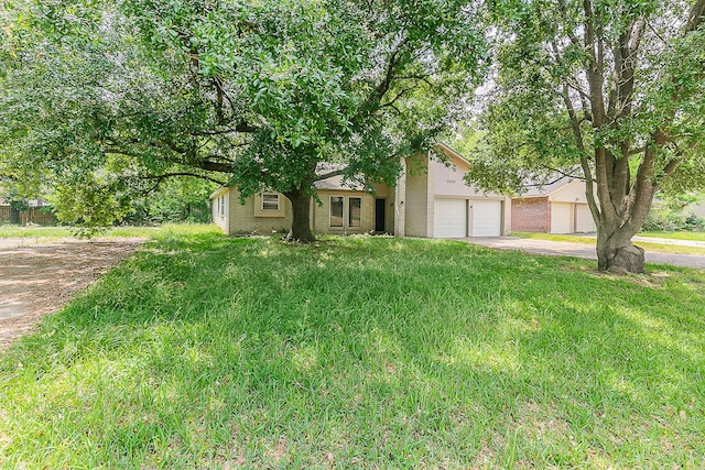 view of property hidden behind natural elements featuring a garage, driveway, and a front lawn