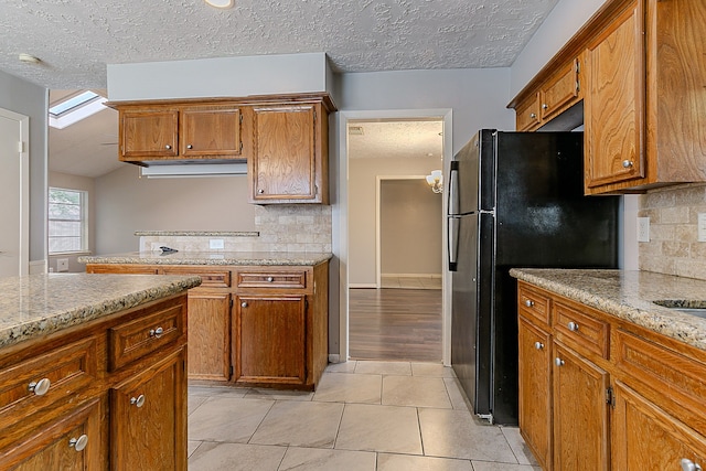 kitchen with brown cabinetry, decorative backsplash, a textured ceiling, and freestanding refrigerator