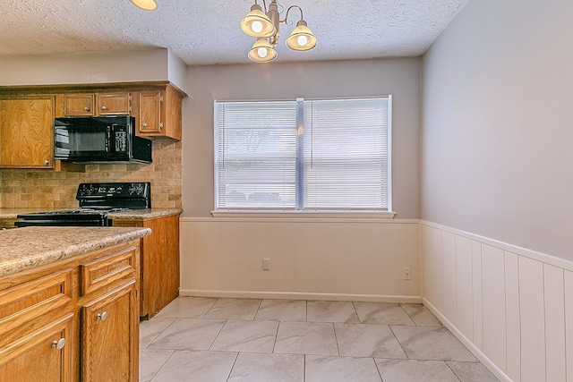 kitchen with brown cabinetry, black appliances, wainscoting, and light countertops