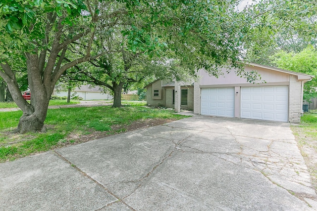 view of property hidden behind natural elements featuring brick siding, a garage, and aphalt driveway