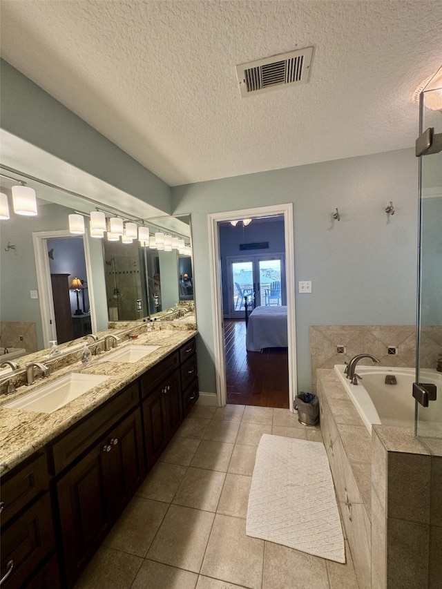 bathroom featuring a textured ceiling, ensuite bath, a bath, double vanity, and tile patterned flooring