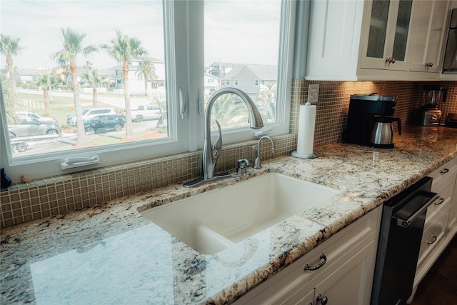 kitchen view of a sink, white cabinets, and backsplash