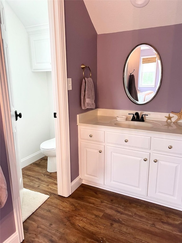 bathroom with toilet, vanity, wood finished floors, and baseboards