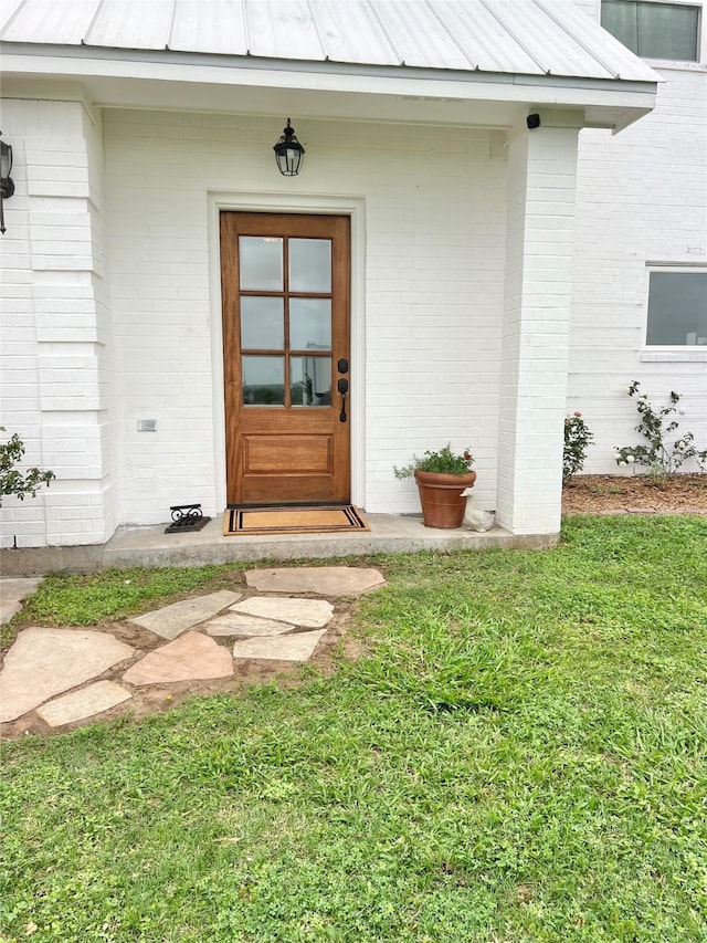 entrance to property featuring brick siding, a yard, a standing seam roof, and metal roof