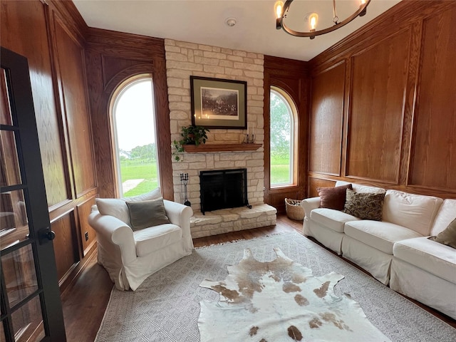 living area featuring plenty of natural light, a stone fireplace, wood finished floors, and an inviting chandelier