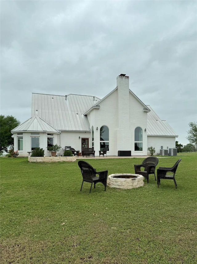 back of house featuring a lawn, a standing seam roof, an outdoor fire pit, and metal roof