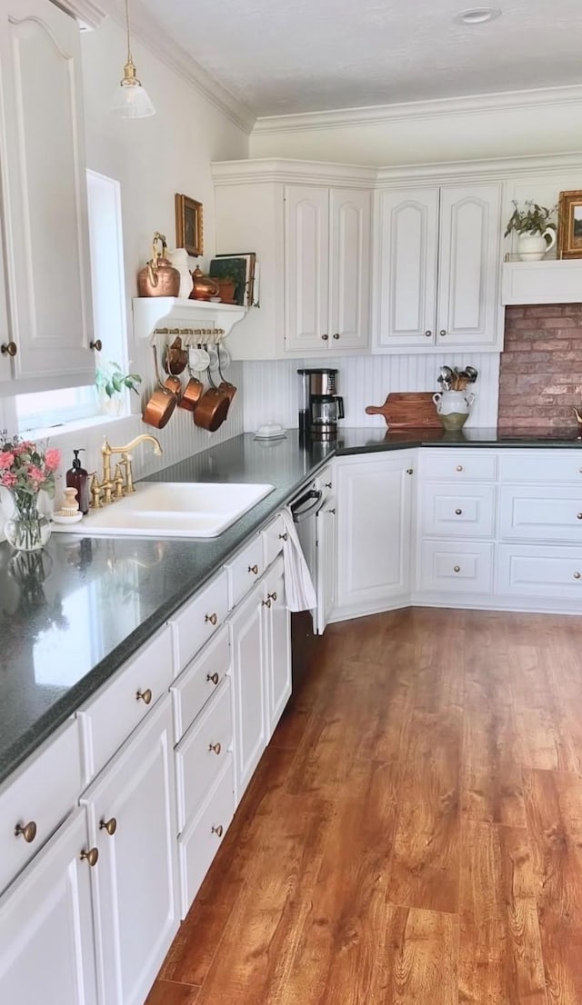 kitchen featuring a sink, light wood-style floors, white cabinetry, pendant lighting, and ornamental molding