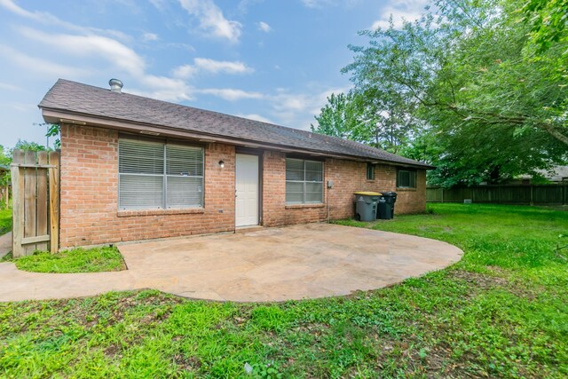 rear view of house with fence, a shingled roof, a patio area, a lawn, and brick siding