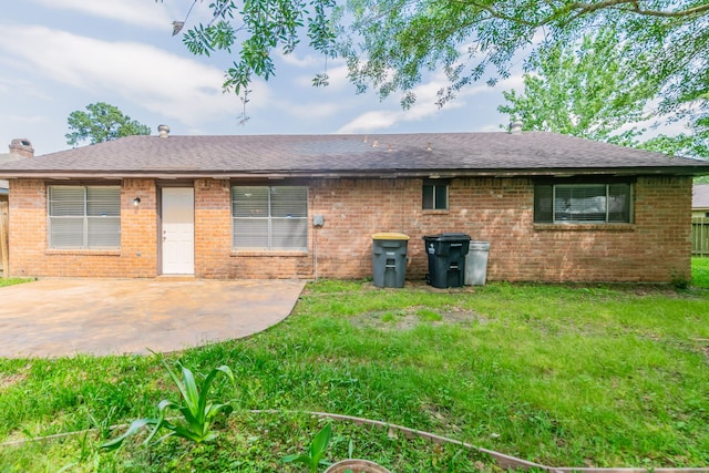 back of property with brick siding, roof with shingles, a patio, and a lawn