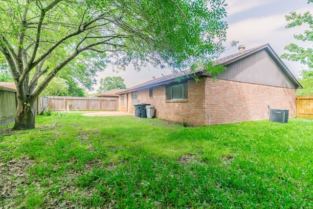 rear view of property with a fenced backyard, brick siding, central air condition unit, and a lawn