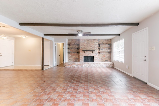 unfurnished living room with a textured ceiling, beam ceiling, baseboards, a brick fireplace, and ceiling fan