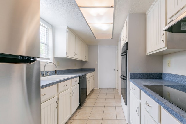 kitchen featuring under cabinet range hood, a sink, light tile patterned flooring, black appliances, and a textured ceiling