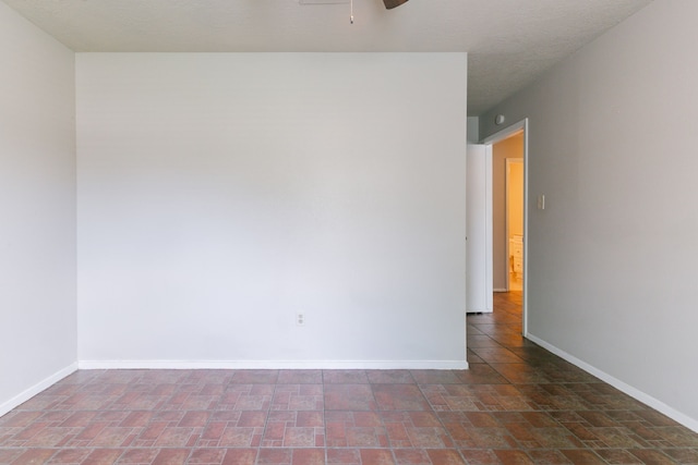 unfurnished room with stone finish flooring, a ceiling fan, and baseboards
