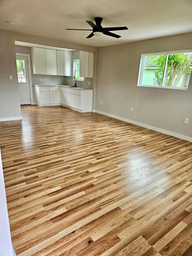 unfurnished living room with ceiling fan, baseboards, a sink, and light wood-style floors