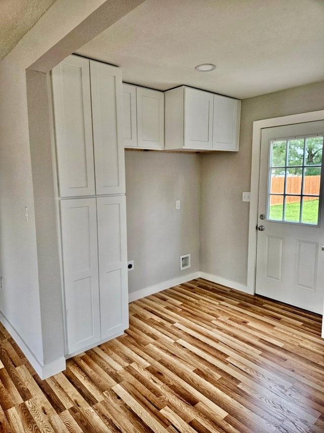 interior space featuring visible vents, light wood-style flooring, baseboards, and white cabinetry